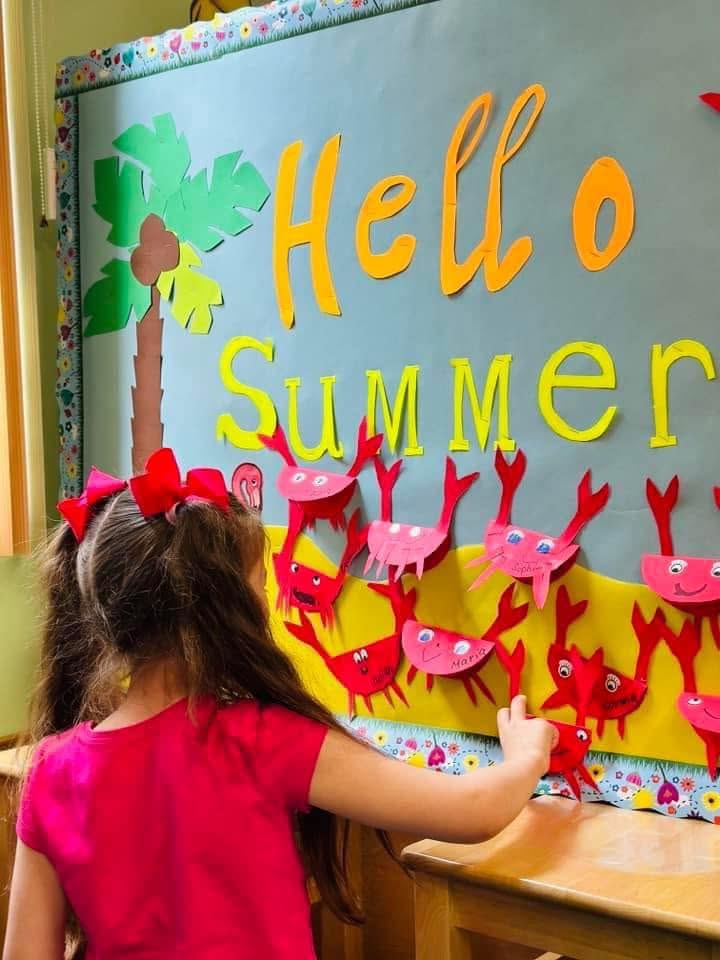 Girl adding paper crabs to a colorful Hello Summer bulletin board