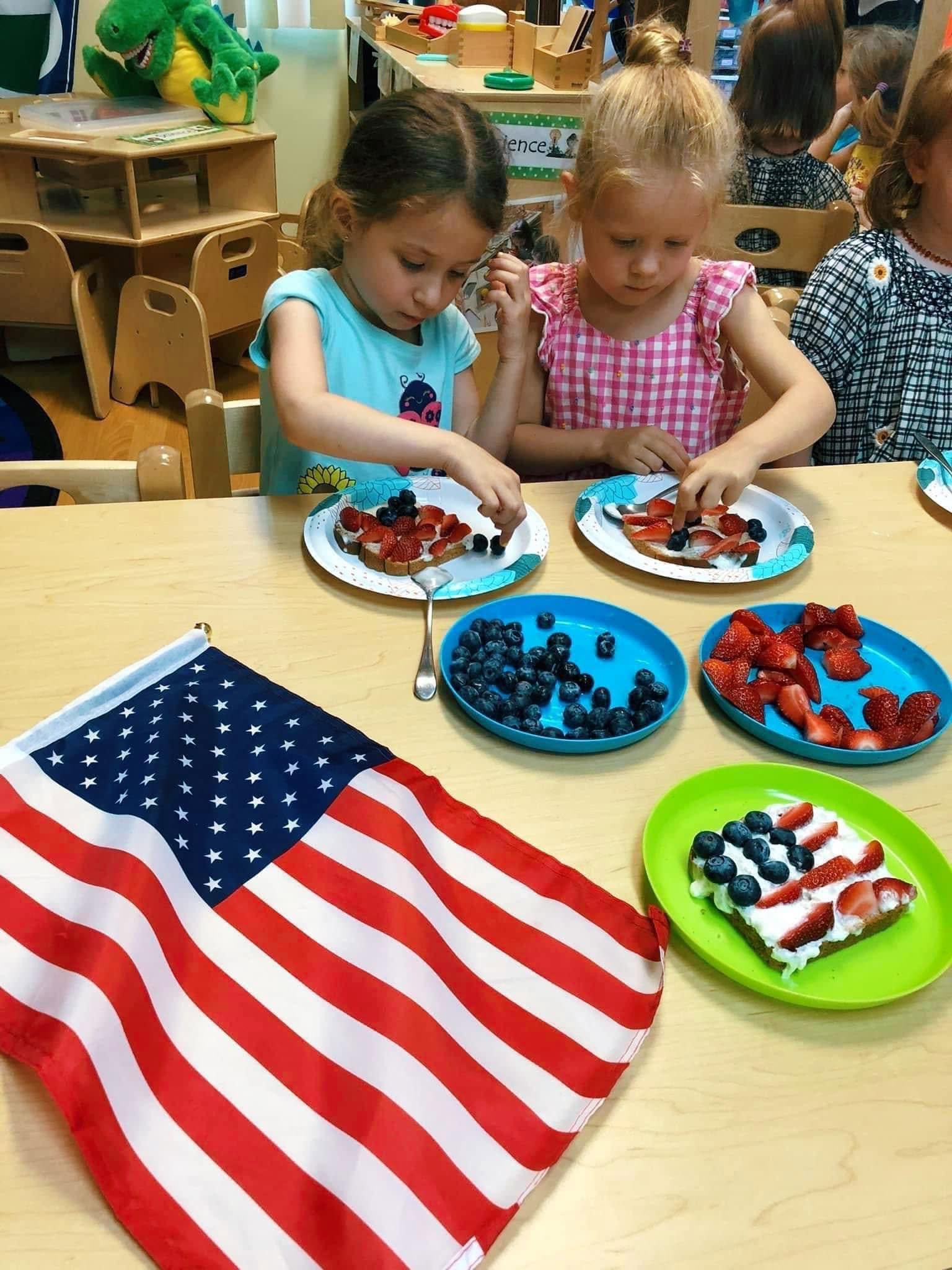 Two girls decorating toast with strawberries and blueberries into a flag pattern