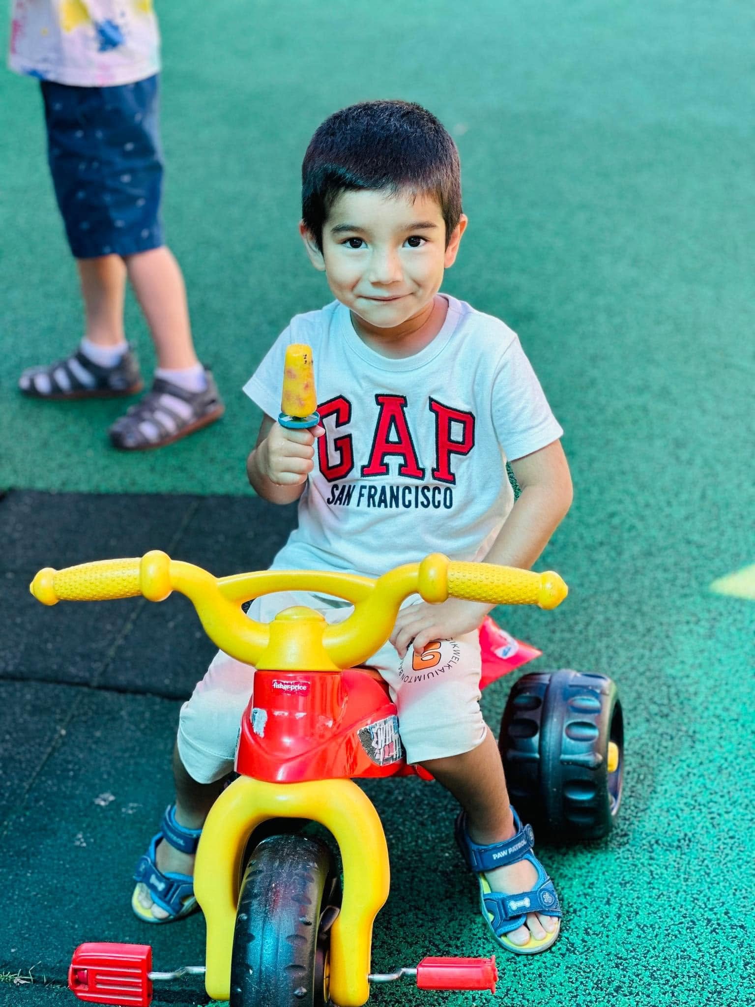 Child enjoying a popsicle on a tricycle at summer camp